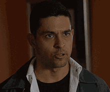 a man wearing a black shirt and a gray jacket is looking at the camera