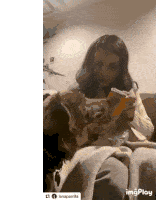 a woman is sitting on a couch with a dog licking her face while holding a can of soda .