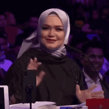 a woman wearing a hijab is sitting in front of a microphone and smiling .