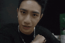 a young man wearing a black shirt and a necklace is smiling