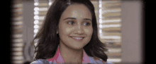 a woman is smiling and looking at the camera in front of a window
