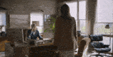 a man sits at a desk with an apple computer and a woman stands in front of him