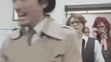 a group of people are standing next to each other in a room . one of the people is wearing a trench coat .