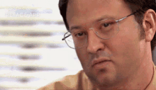 a man wearing glasses is making a funny face while sitting in front of a window .