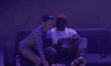 a man and a woman are sitting on a couch in a dark room with purple lights .