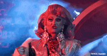 a drag queen wearing a wig and earrings is making a funny face .