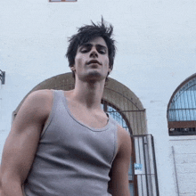 a young man wearing a grey tank top stands in front of a white building