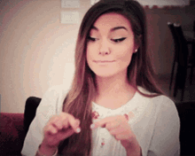 a woman with long hair is sitting on a couch and looking at her nails