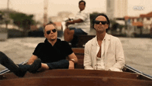 two men wearing sunglasses are sitting on a boat with the word max on the bottom right