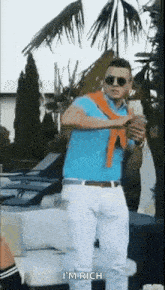 a man in a blue shirt and white pants is standing in front of a palm tree holding a bottle of water .