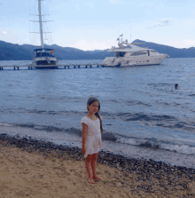 a little girl stands on the beach in front of a large boat