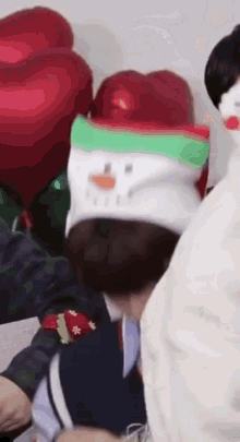 a group of people are sitting around a table with balloons and a snowman hat .