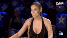 a woman wearing a braided ponytail is sitting in front of a microphone in front of a deluxe sign