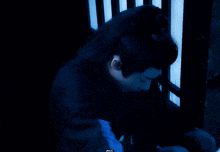 a man with long black hair is sitting in a dark room with a blue light behind him .