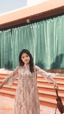 a woman in a dress is standing in front of a green curtain and a green building
