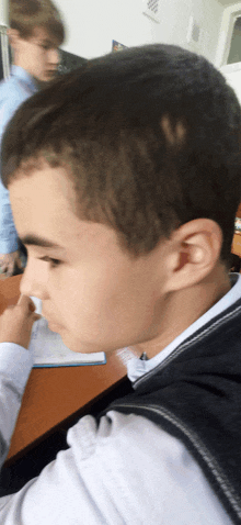 a young boy sits at a desk in a classroom looking down