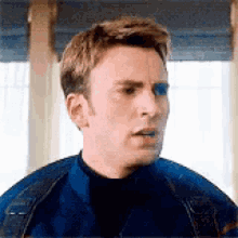 a man in a blue jacket is standing in front of a window and making a funny face .