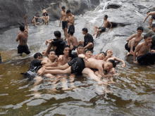 a group of young men are laying in the water and one of them is wearing a black shirt that says ' adidas '