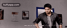 a man is standing in front of a wall with posters on it and talking to another man .