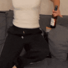 a person is kneeling on a couch holding a bottle of alcohol