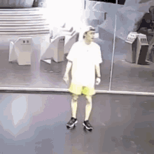 a man in a white shirt and yellow shorts is standing in front of a mirror in a room .