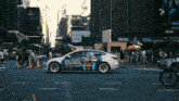 a tesla model 3 is driving down a city street with an advertisement on the side