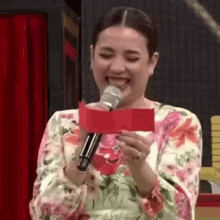 a woman is laughing while holding a microphone and a piece of paper .