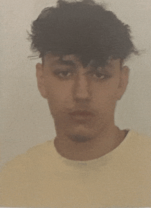 a young man with curly hair is wearing a yellow sweater