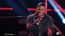 a man is singing into a microphone with the words #thevoice behind him