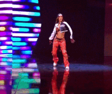 a woman is dancing on a stage in front of a colorful background of lights .