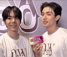 two young men standing next to each other holding a secret news card
