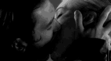 a man and a woman are kissing in a black and white photo . the woman is touching the man 's face .
