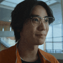 a man wearing glasses and an orange jacket looks to the side