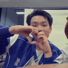 a young man in a blue jacket is making a heart with his hands