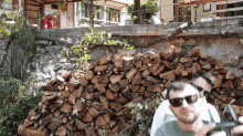 two men wearing sunglasses are standing in front of a pile of wood