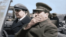 two men in hats are sitting in a car and one is covering his mouth
