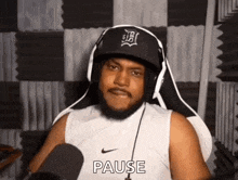 a man wearing headphones and a hat is sitting in front of a microphone and making a pause sign .