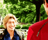 a man in a red jacket is smiling at another man in a blue shirt