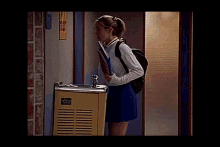 a girl in a cheerleader uniform is standing in front of a water fountain holding a book .