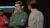 a man in a green shirt is standing next to another man in a floral shirt