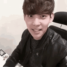 a young man wearing a black leather jacket is sitting in a chair and smiling .