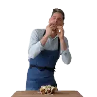 a man in a blue apron is eating tacos on a cutting board