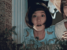 a girl in a blue shirt with bananas on it makes a surprised face