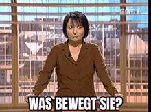 a woman in a brown suit is standing in front of a window with her hands on her hips .