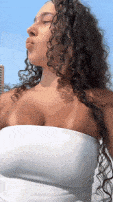 a woman with curly hair is wearing a white strapless top and a white dress .