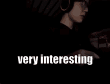 a man wearing headphones and glasses is playing a video game and the words very interesting are on the screen .