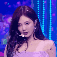 a woman wearing a purple top and earrings is standing in front of a blue background .