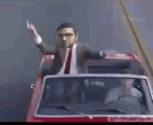 a man in a suit and tie is sitting in a red car with his arms outstretched