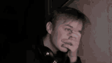 a young man wearing headphones looks at the camera with his hand on his chin