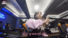 a woman in a pink sweater is sitting in front of a keyboard in a room with a sign that says " play order "